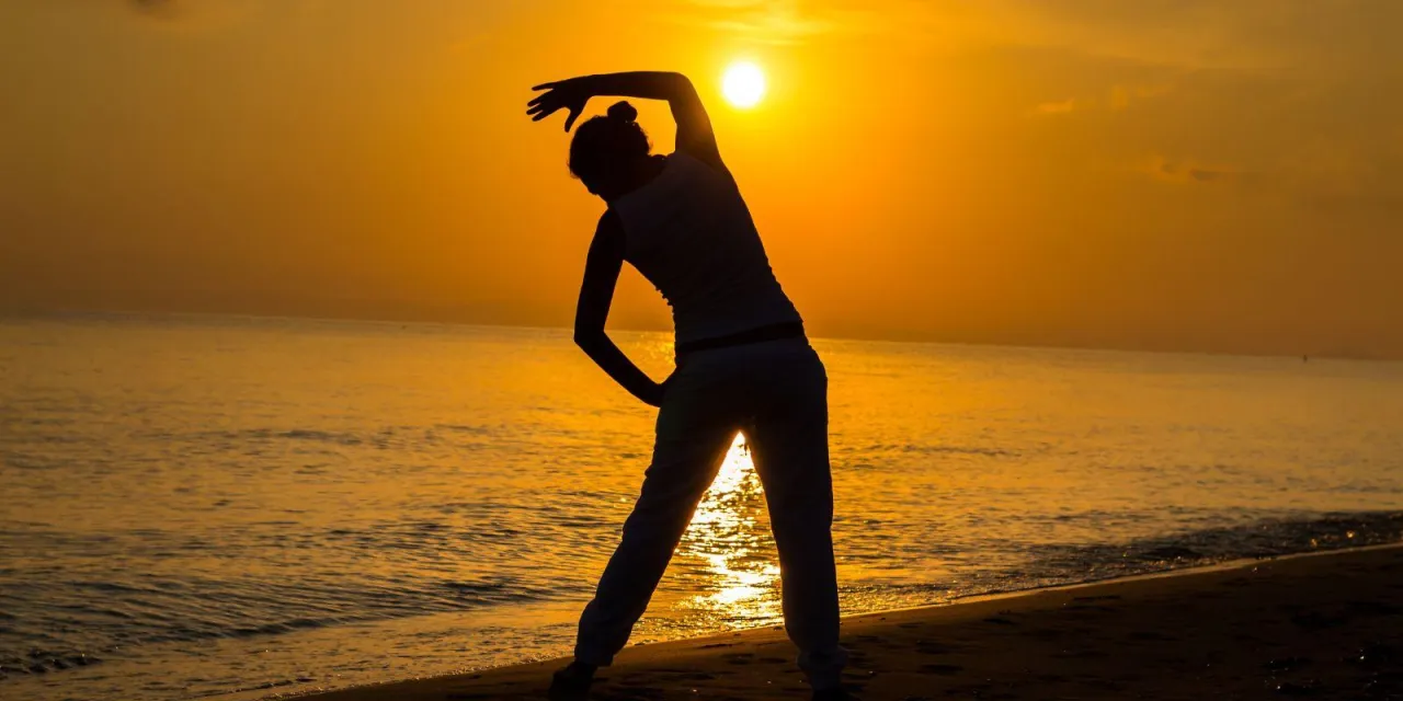 Osoba ćwicząca na siłowni wcześnie rano, wsch&oacute;d słońca za oknem