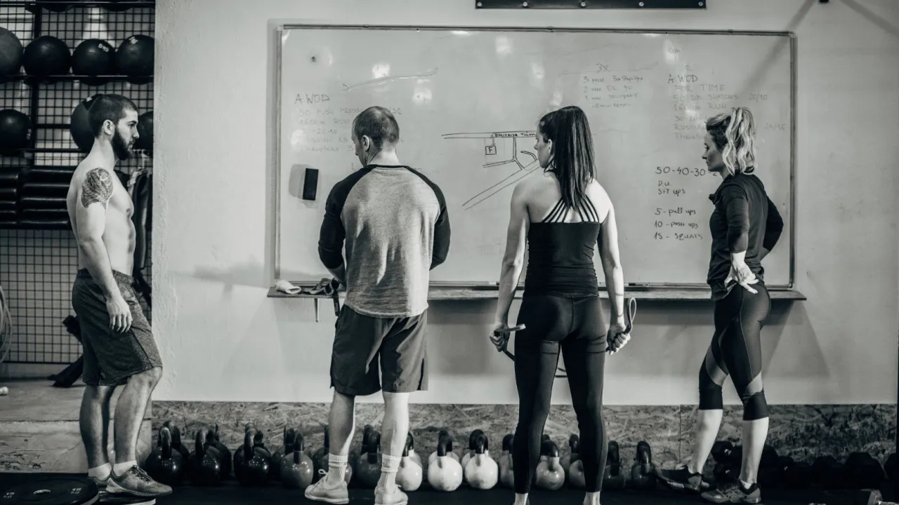 Trening na redukcji: ile razy w tygodniu cardio? Grupa os&oacute;b analizuje plan treningowy na tablicy w siłowni.