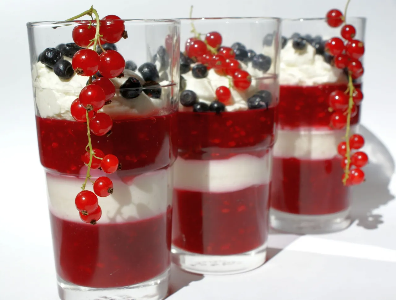 Warstwowy deser w szklankach z bitą śmietaną, musem z czerwonych porzeczek i borówkami. Gałązka czerwonych porzeczek ozdabia deser, pokazując, jak mrozić czerwone porzeczki.