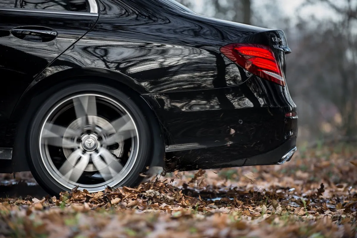 Błyszczący, czarny Mercedes-Benz Klasa E mija jesienne liście, koło w ruchu.