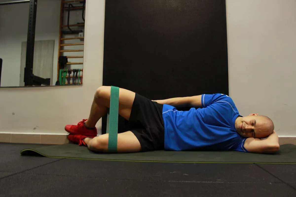 Mężczyzna wykonuje ćwiczenie z gumą oporową na udach. To przykład treningu oporowego co to jest i jak go wykonywać.