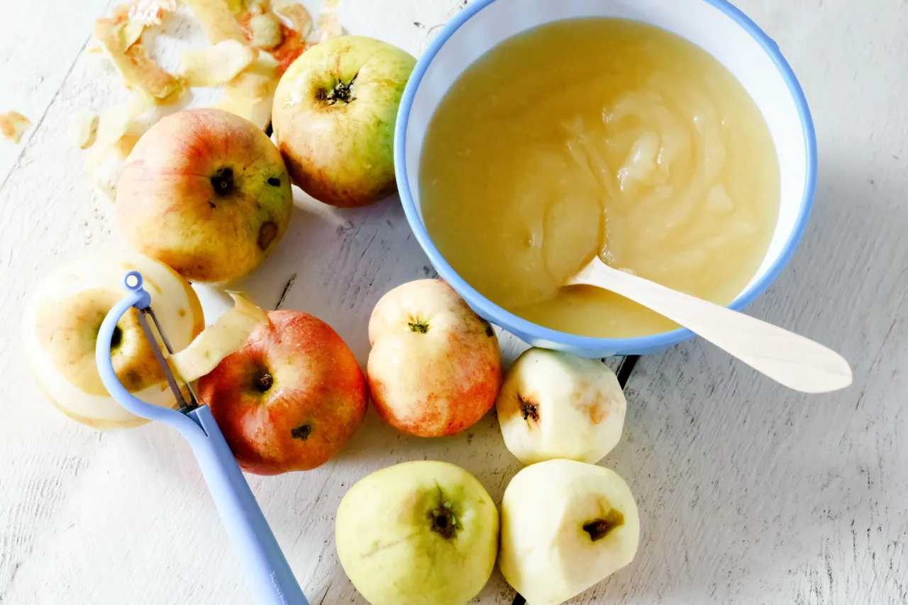 Jak zrobić mus jabłkowy do szarlotki? Jabłka, obieraczka i gotowy mus w miseczce.