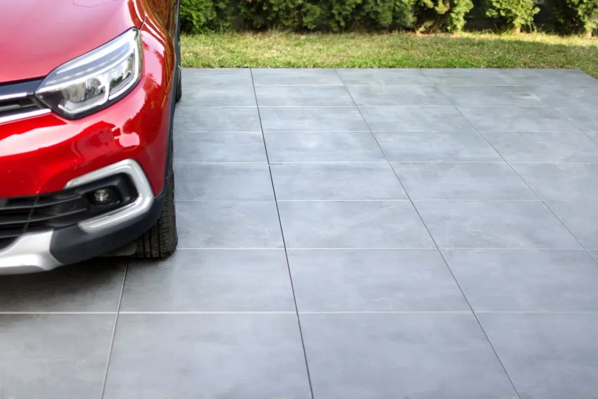 Nowoczesne, szare płytki na podjazd, idealne dla Twojego czerwonego samochodu.