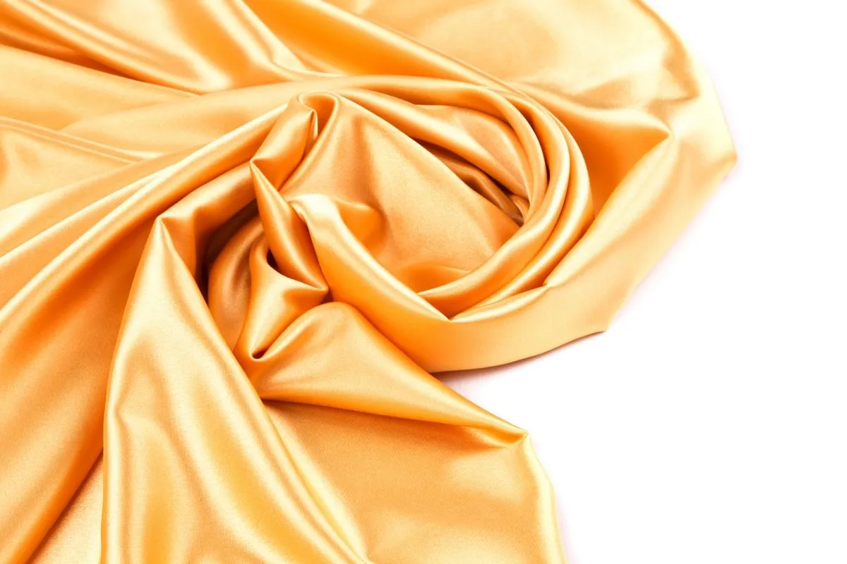 Złoty, połyskliwy sztuczny jedwab układa się w miękkie fałdy, tworząc elegancką draperię.