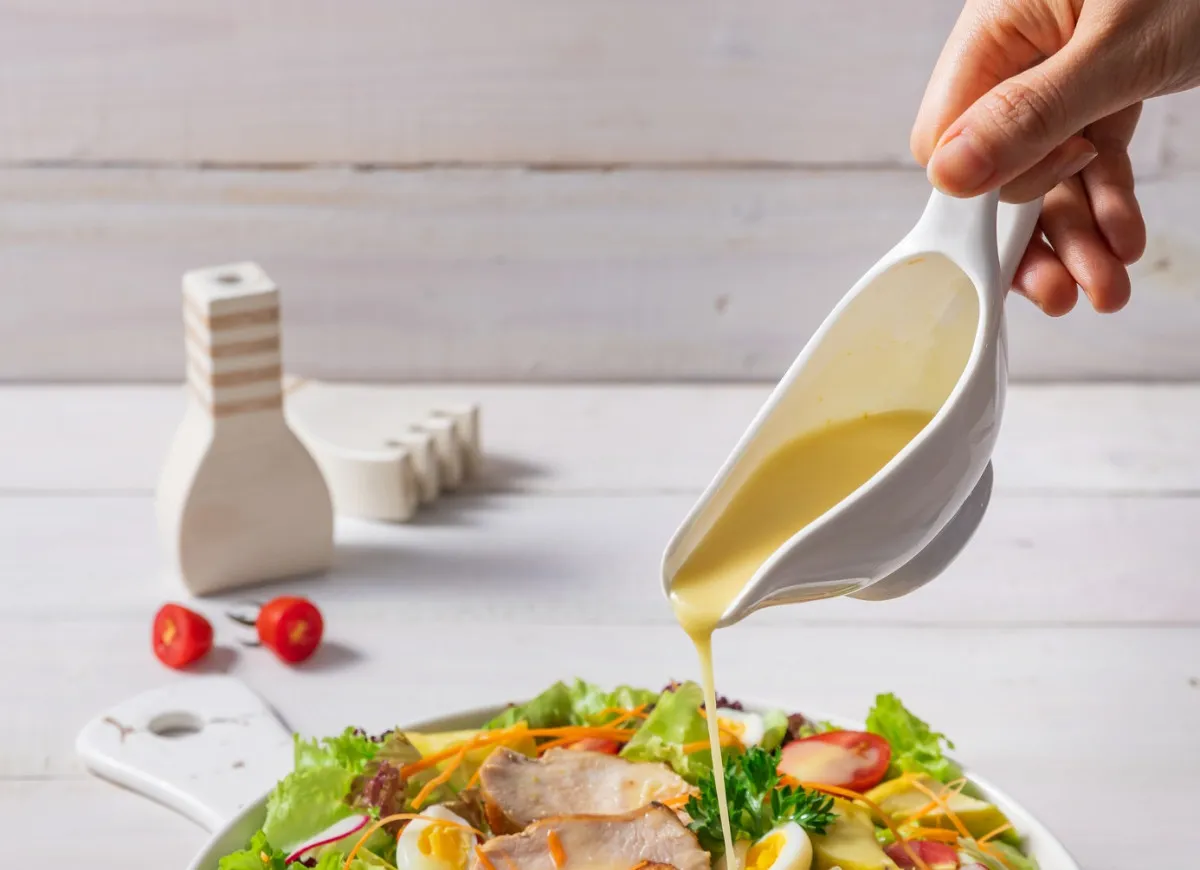 Jak zrobić sos do sałatki z oleju? Delikatny, ż&oacute;łty sos spływa z sosjerki na świeżą sałatkę z kurczakiem i jajkiem.