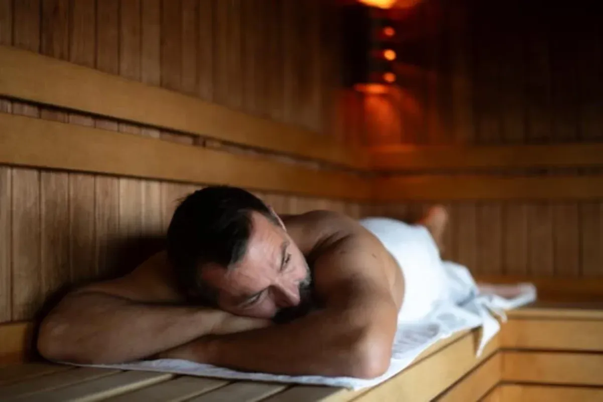 Mężczyzna odpoczywa w saunie po treningu. Czy sauna po treningu jest zdrowa? Relaks w drewnianej kabinie.