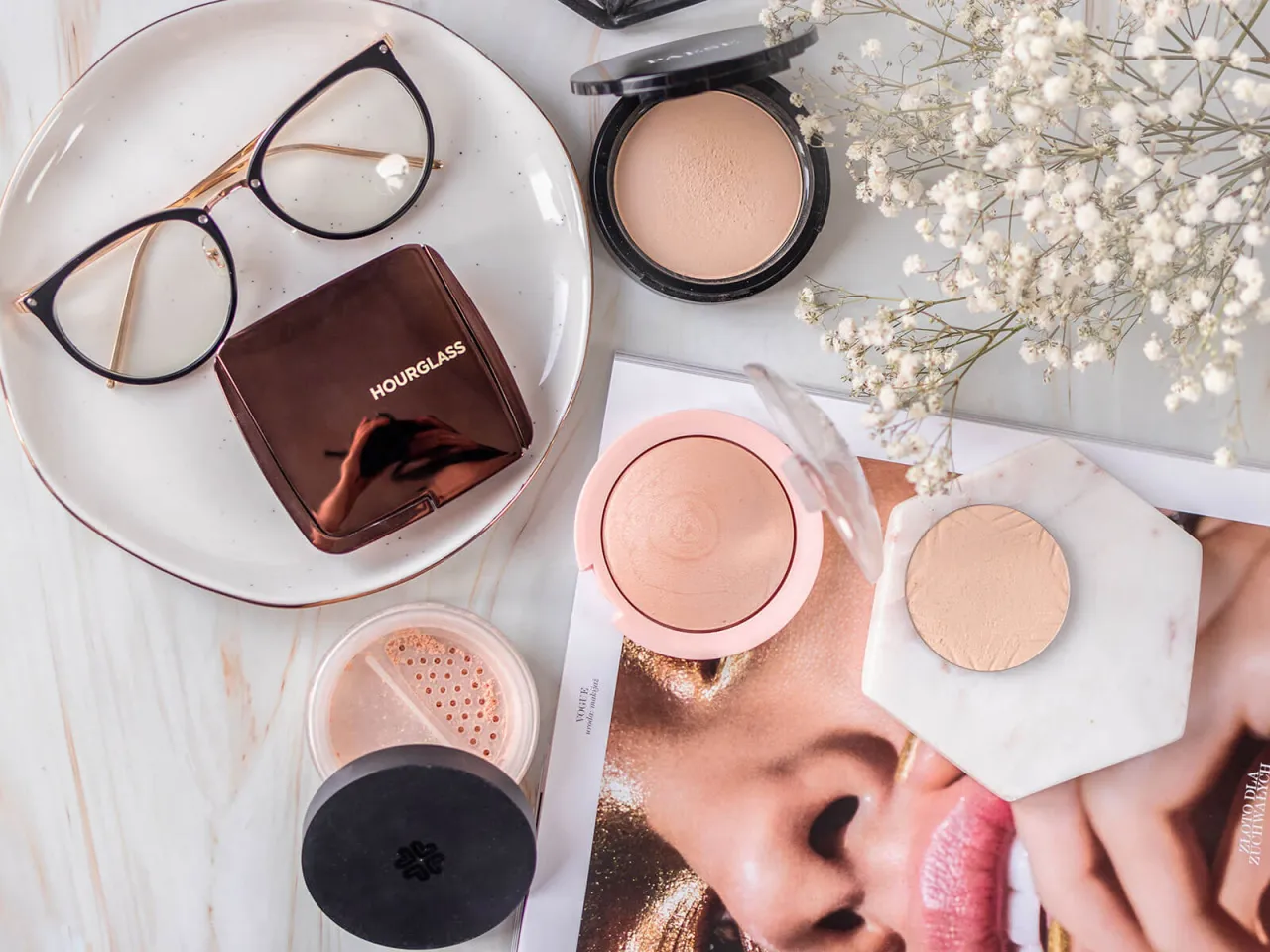 Puder rozświetlający na całą twarz, kosmetyki i okulary na marmurowym tle.