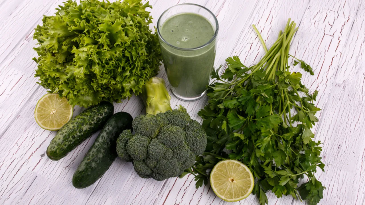 Zielony koktajl z blendera, obok świeżej sałaty, brokułów, ogórków, natki pietruszki i limonki. Idealne składniki na przepisy na zdrowe koktajle z blendera.