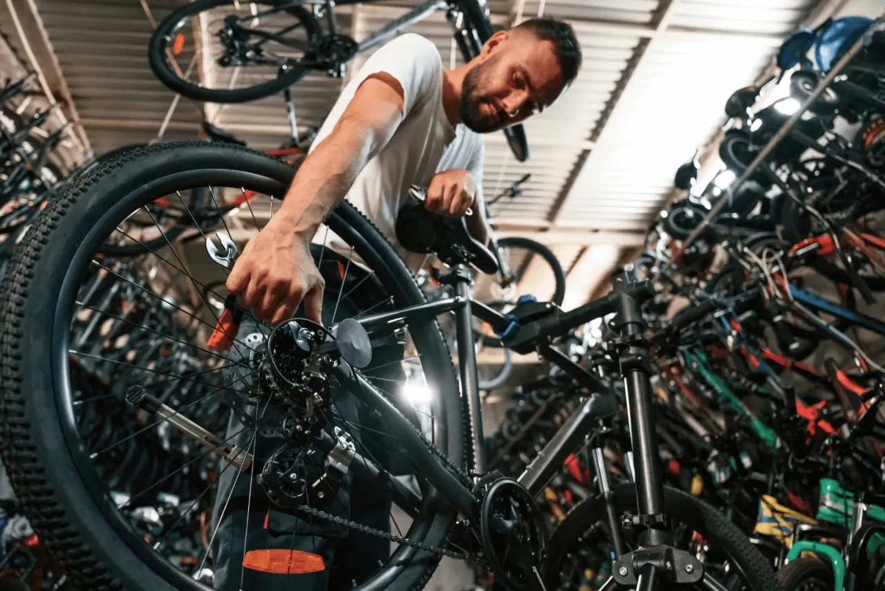 Mechanik pokazuje, jak założyć tylne koło w rowerze z przerzutkami, używając klucza do dokręcenia osi.