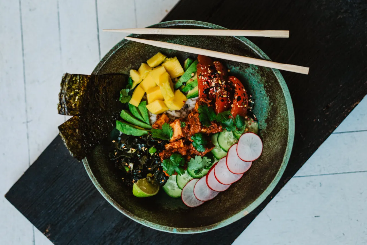 Kolorowa miska pełna zdrowych składnik&oacute;w: ryż, awokado, mango, og&oacute;rek, rzodkiewka, wodorosty i pieczona papryka. Idealna odpowiedź na pytanie: dieta wegańska co jeść.