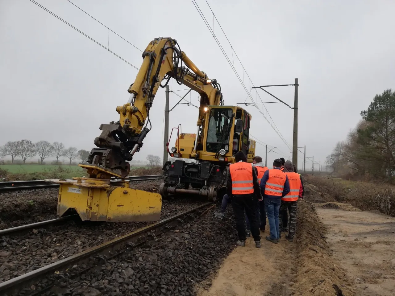 Grupa operatorów w kamizelkach obserwuje pracę koparki na torach. Czy kurs na koparkę jest trudny? To zależy od zaangażowania!