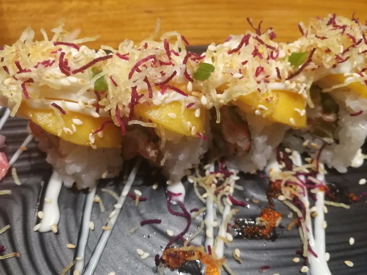 Rolka sushi z kawałkami mango, kremowym sosem, chrupiącą posypką i sezamem.