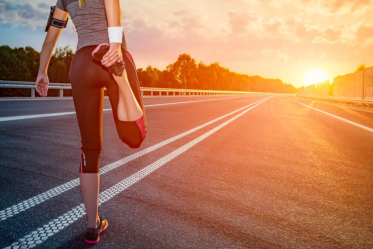 Kobieta rozciąga się na pustej drodze o zachodzie słońca. Posiłek przed treningiem ile czasu? Czas na bieganie!
