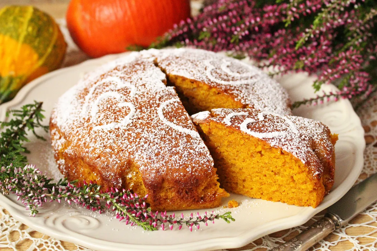 Pyszne ciasto dyniowe okrasa łamie przepisy, posypane cukrem pudrem z serduszkami. Obok dynie i wrzosy.