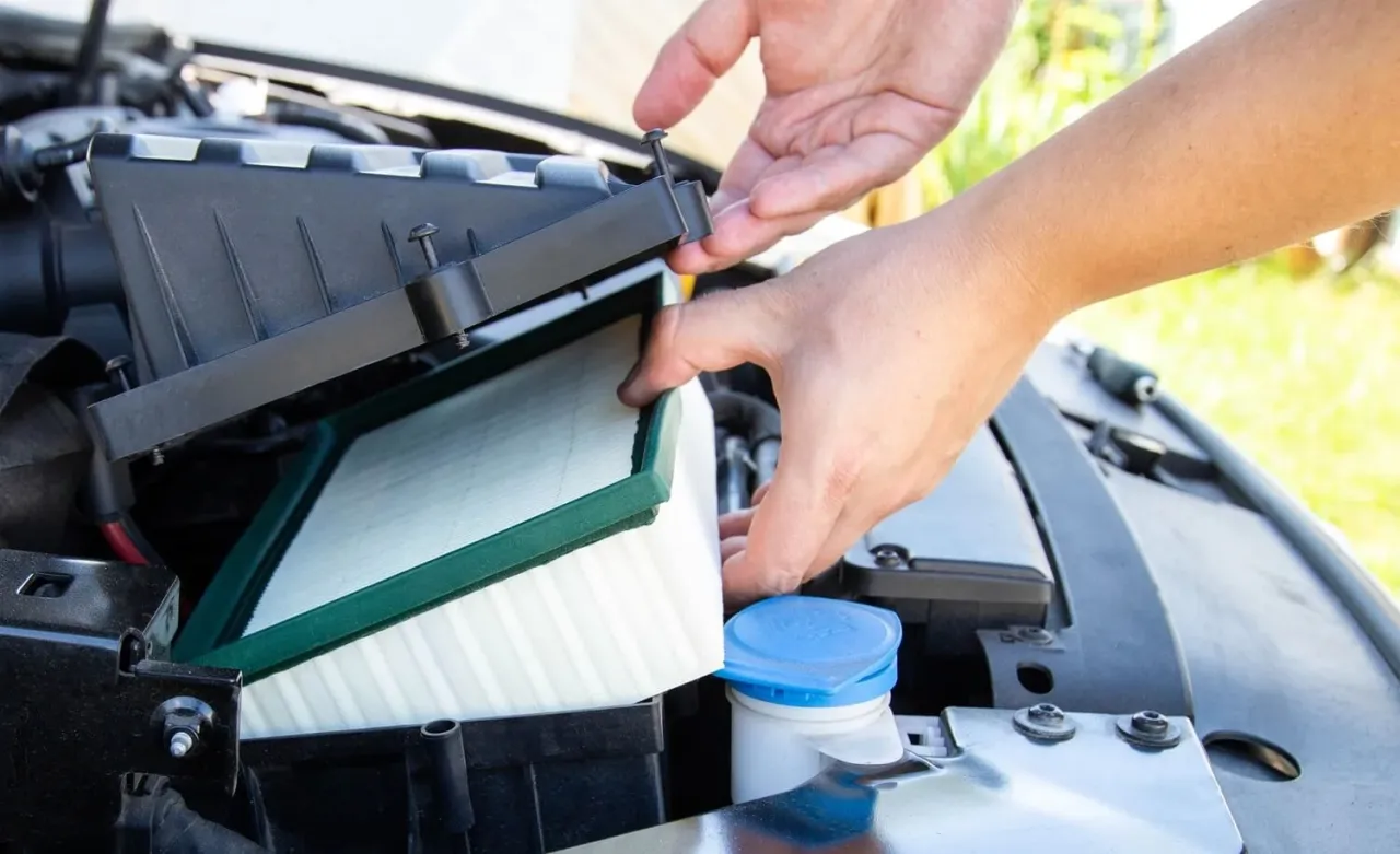 Wymiana filtra powietrza w samochodzie. Dłonie montują nowy, biały filtr z zieloną ramką w czarnej obudowie.