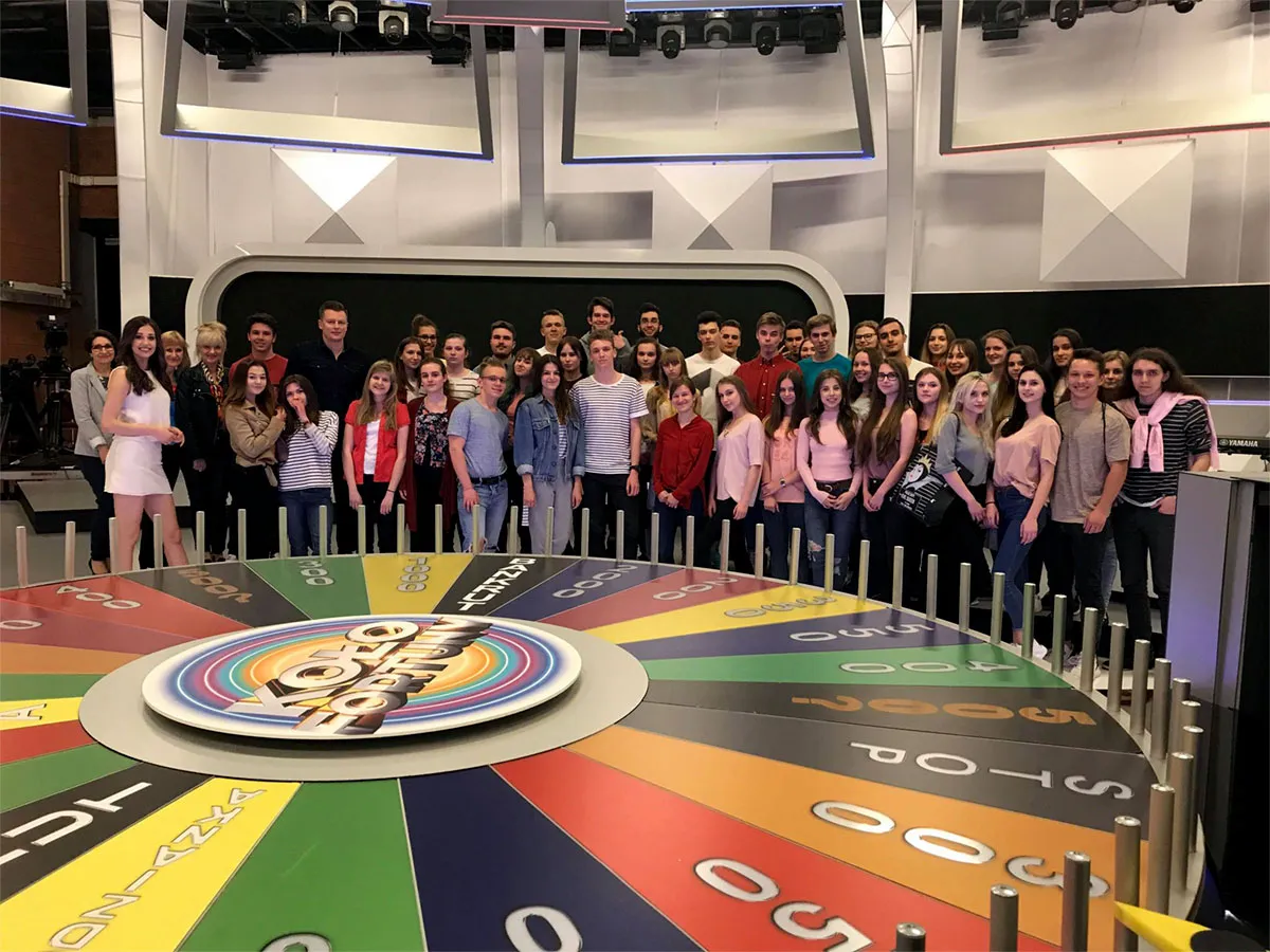 Grupa ludzi pozuje do zdjęcia przy wielkim kole fortuny, gdzie jest nagrywane.