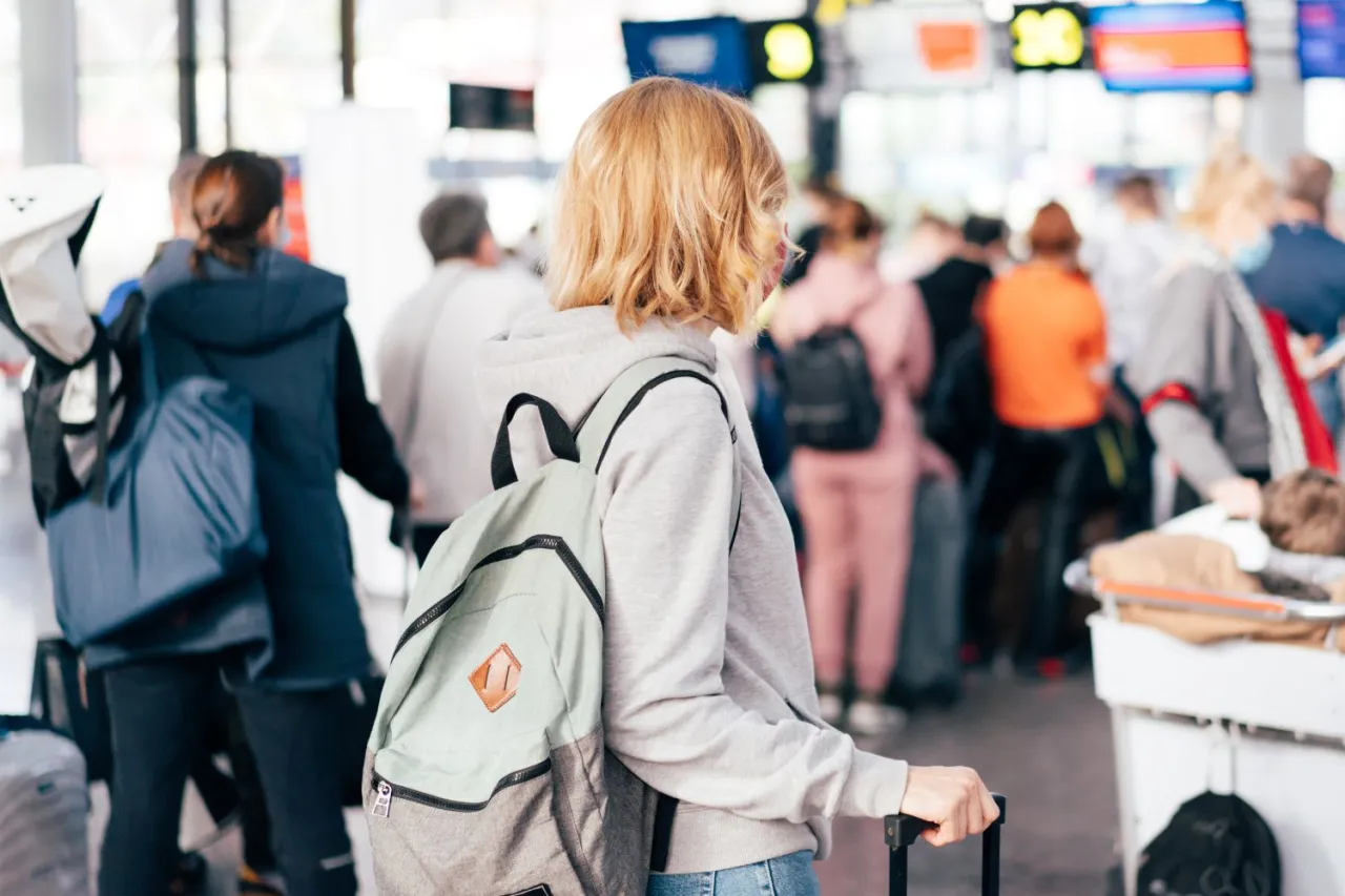 Osoby w tłumie na lotnisku, z plecakami i walizkami. Turystyczny fundusz gwarancyjny co to? Bezpieczeństwo podróży.