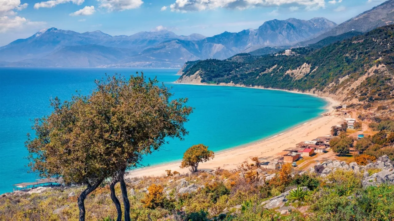 Widok na zatokę z turkusową wodą i piaszczystą plażą, otoczoną zielonymi wzg&oacute;rzami i g&oacute;rami. To jedno z najpiękniejszych miejsc w Albanii.