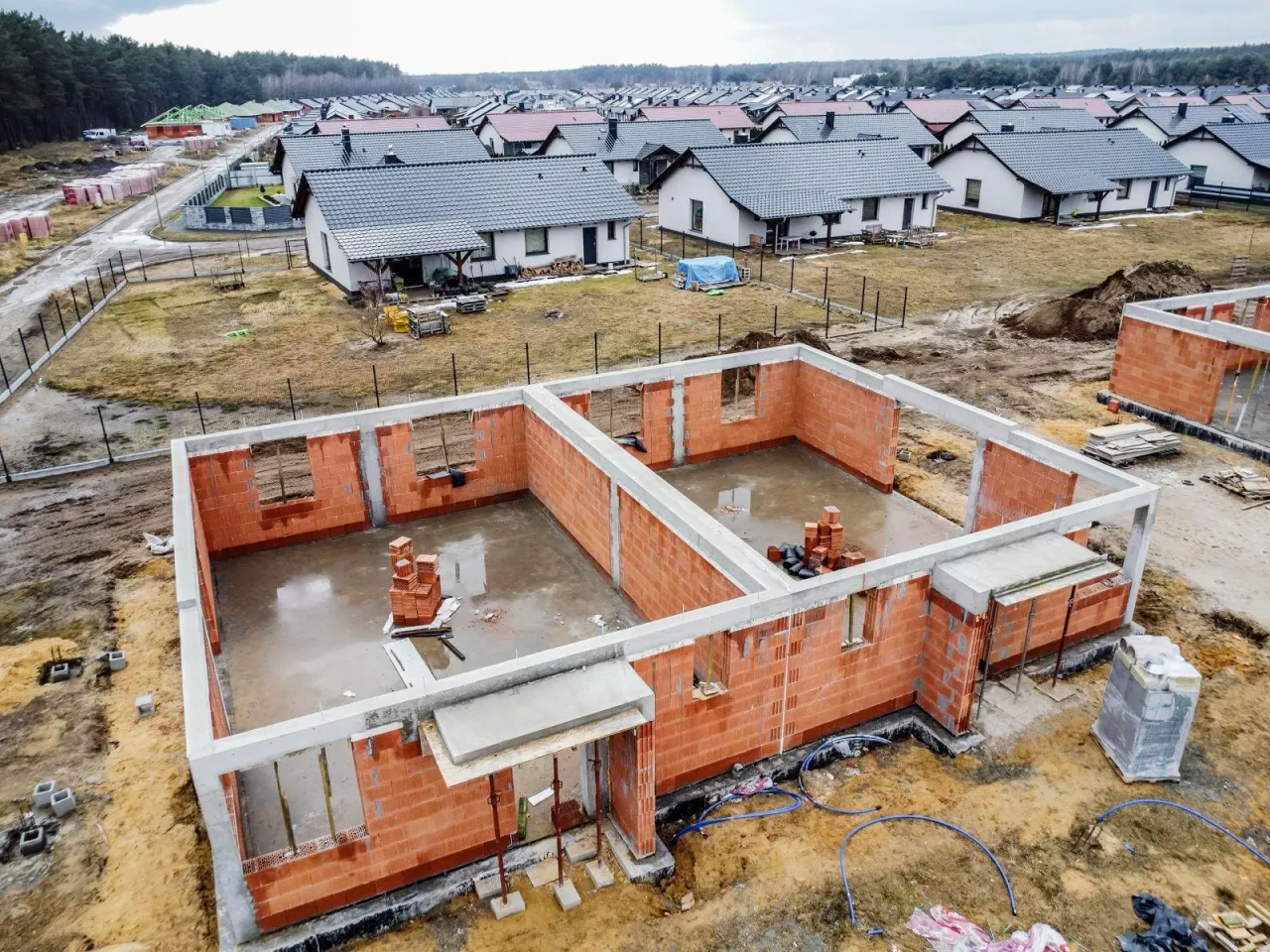 Budowa domu od podstaw, jak zostać deweloperem. Fundamenty i ściany z cegły, w tle osiedle domów.