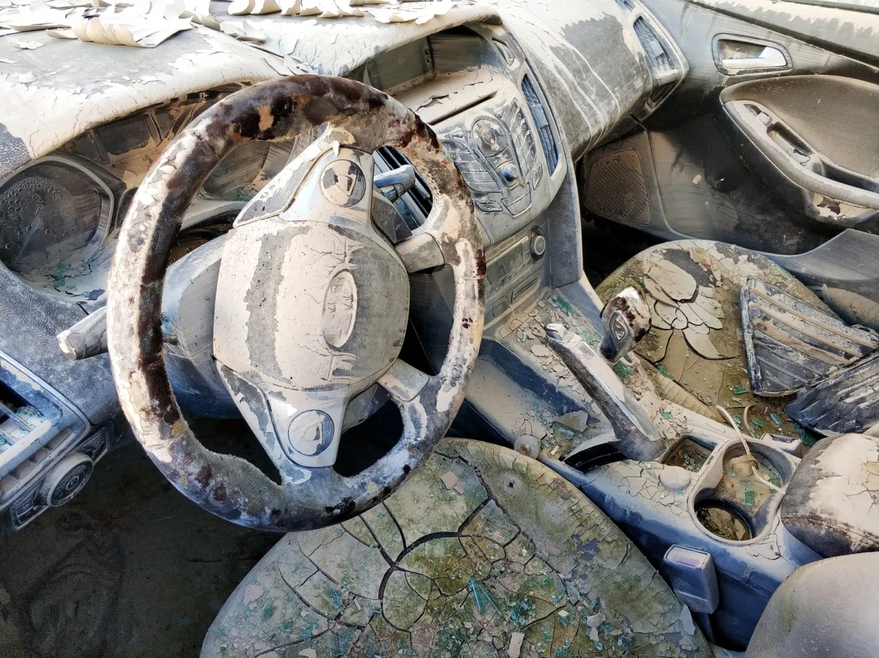 Wnętrze zniszczonego auta po powodzi. Kierownica, deska rozdzielcza i siedzenia pokryte grubą warstwą błota i łuszczącej się farby.