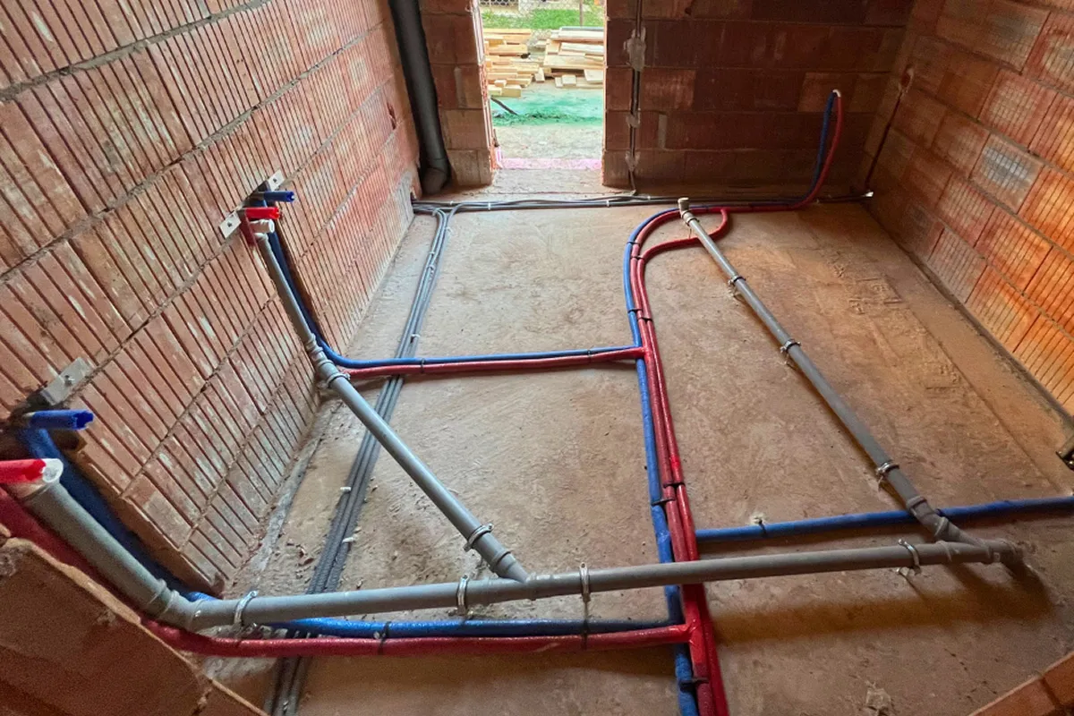 Instalacja hydrauliczna w domu: czerwone i niebieskie rury wodne biegnące po betonowej podłodze i ceglanych ścianach.