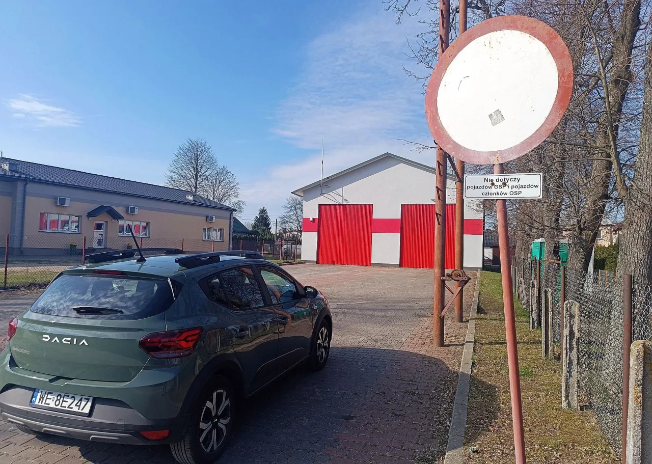 Zielony Dacia Sandero stoi przed remizą OSP. Znak zakazu ruchu z tabliczką 