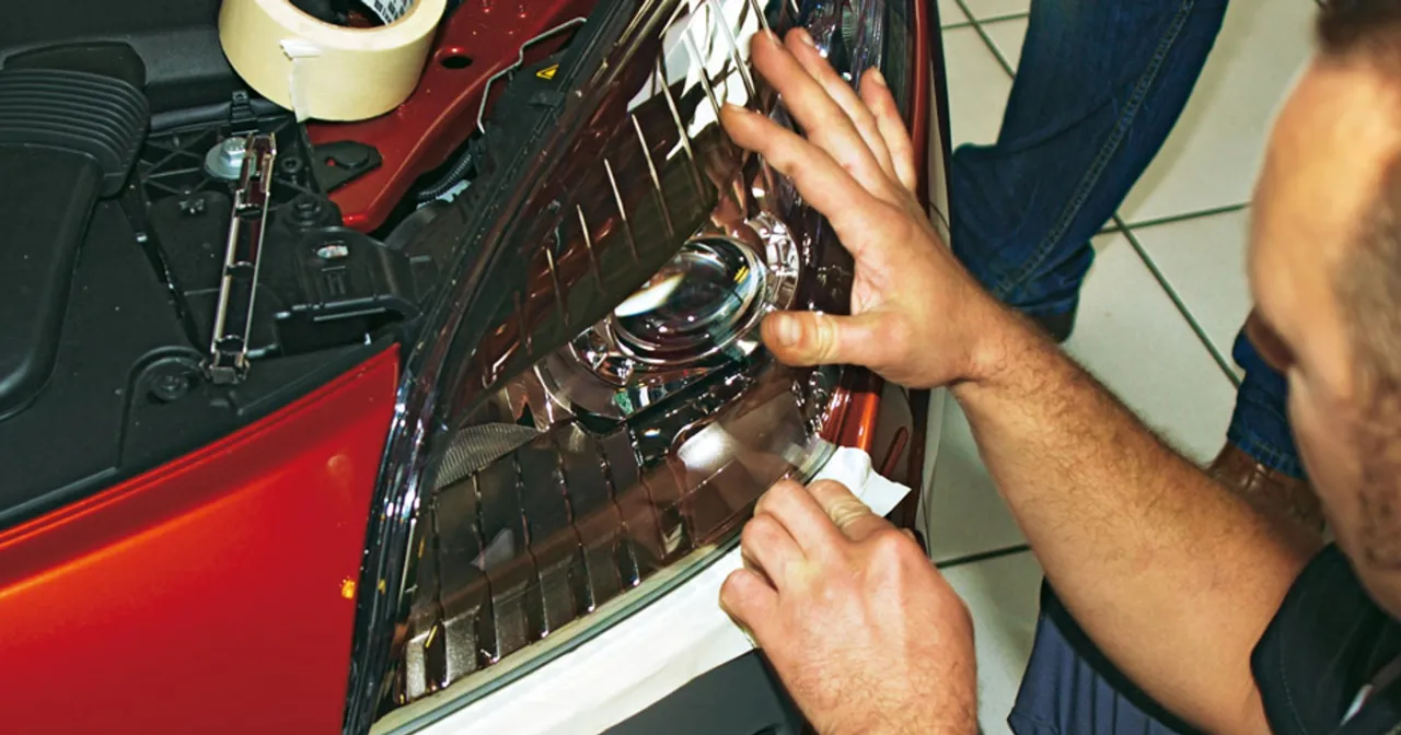 Mężczyzna zakleja taśmą maskownicę reflektora, przygotowując się do wymiany żar&oacute;wki w samochodzie.