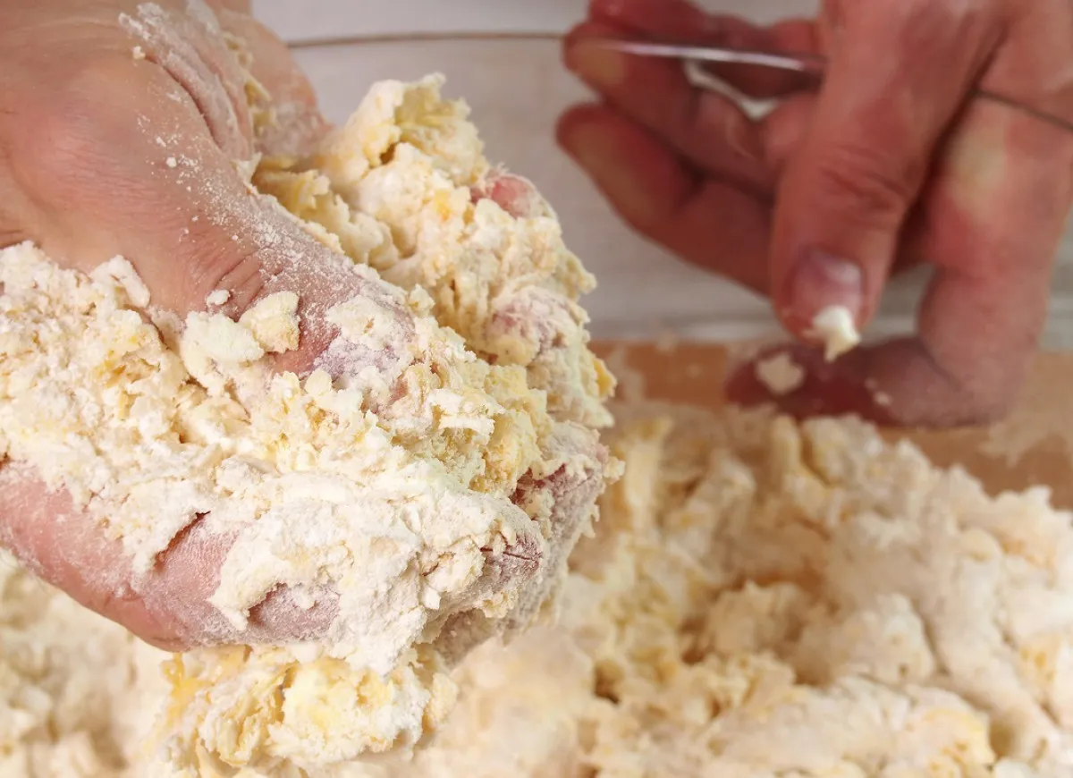 Ręce zagniatają kruche ciasto. Czy do kruchego ciasta daje się proszek do pieczenia? To pytanie nurtuje wielu piekarzy.