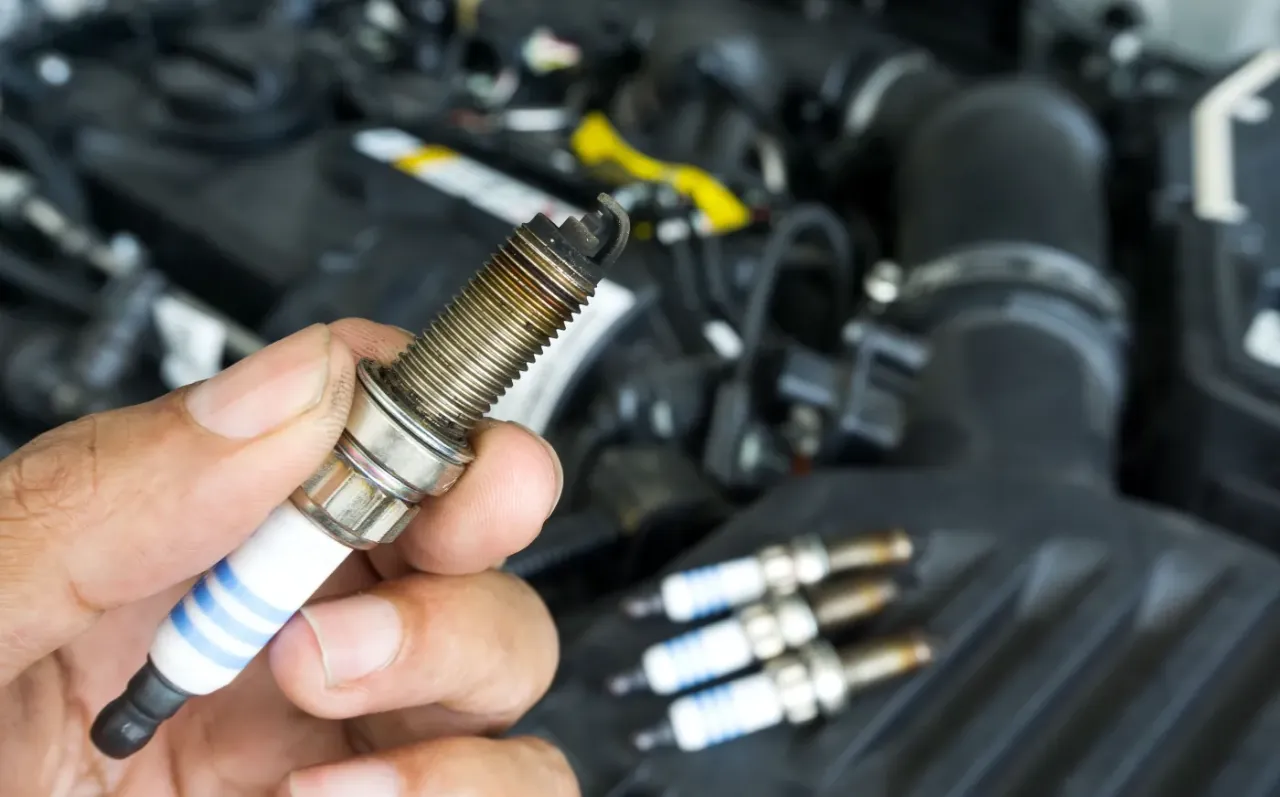 Dłoń trzyma zużytą świecę zapłonową, obok leżą kolejne. Czas na wymianę świec w benzynie?