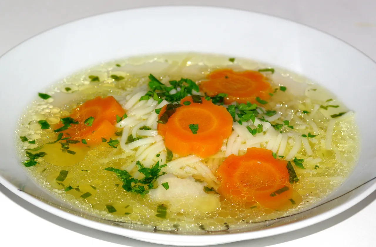 Aksamitny rosół wołowo-drobiowy czy czysty wywar z kury? Z makaronem, marchewką i natką pietruszki, podany w białej misce.