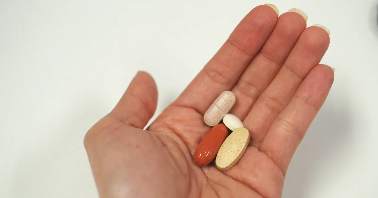 Dłoń trzyma kilka tabletek, w tym te potrzebne do suplementacji żelaza.