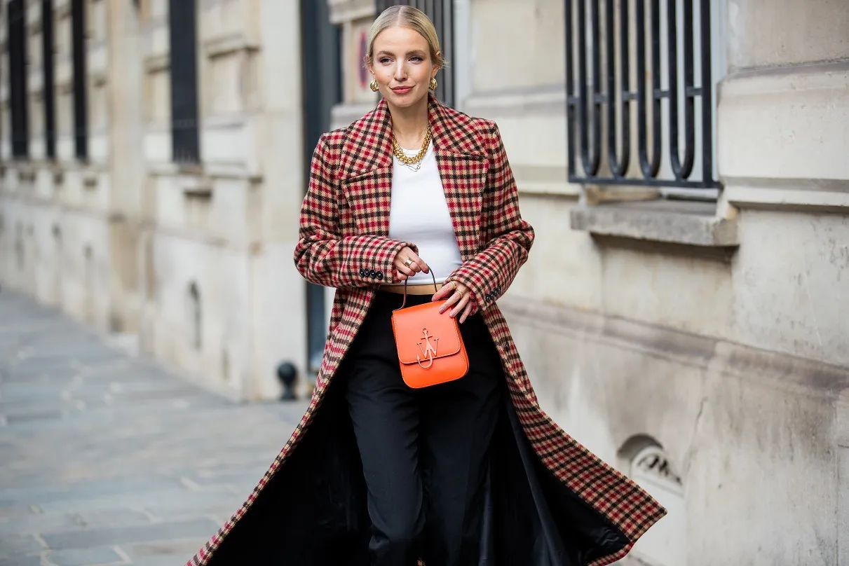 Elegancka kobieta w długim, czerwono-beżowym płaszczu w kratę, z pomarańczową torebką.