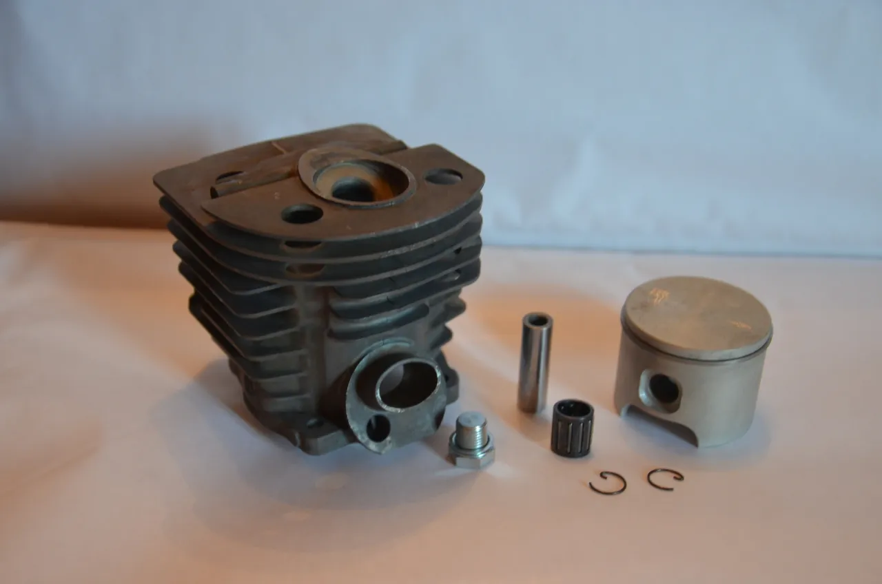 Części motocyklowe Husqvarna: cylinder, tłok, sworzeń, łożysko igiełkowe, śruba i zabezpieczenia.