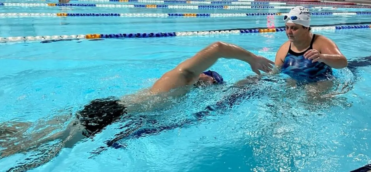 Instruktorka pokazuje, jak nauczyć się dobrze pływać, pomagając pływakowi w basenie.