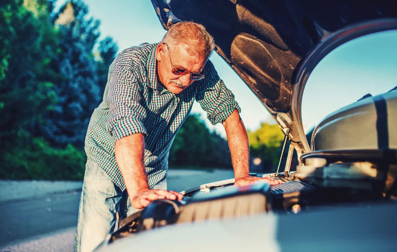 Mężczyzna z wąsem i okularami sprawdza silnik auta. Zastanawia się, co obejmuje HDI AC serwis, gdy auto ulegnie awarii.