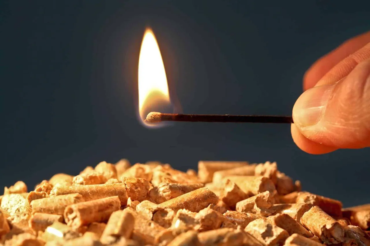 Zapalona zapałka zbliża się do sterty pelletu. To paliwo stałe, ekologiczne i wydajne.