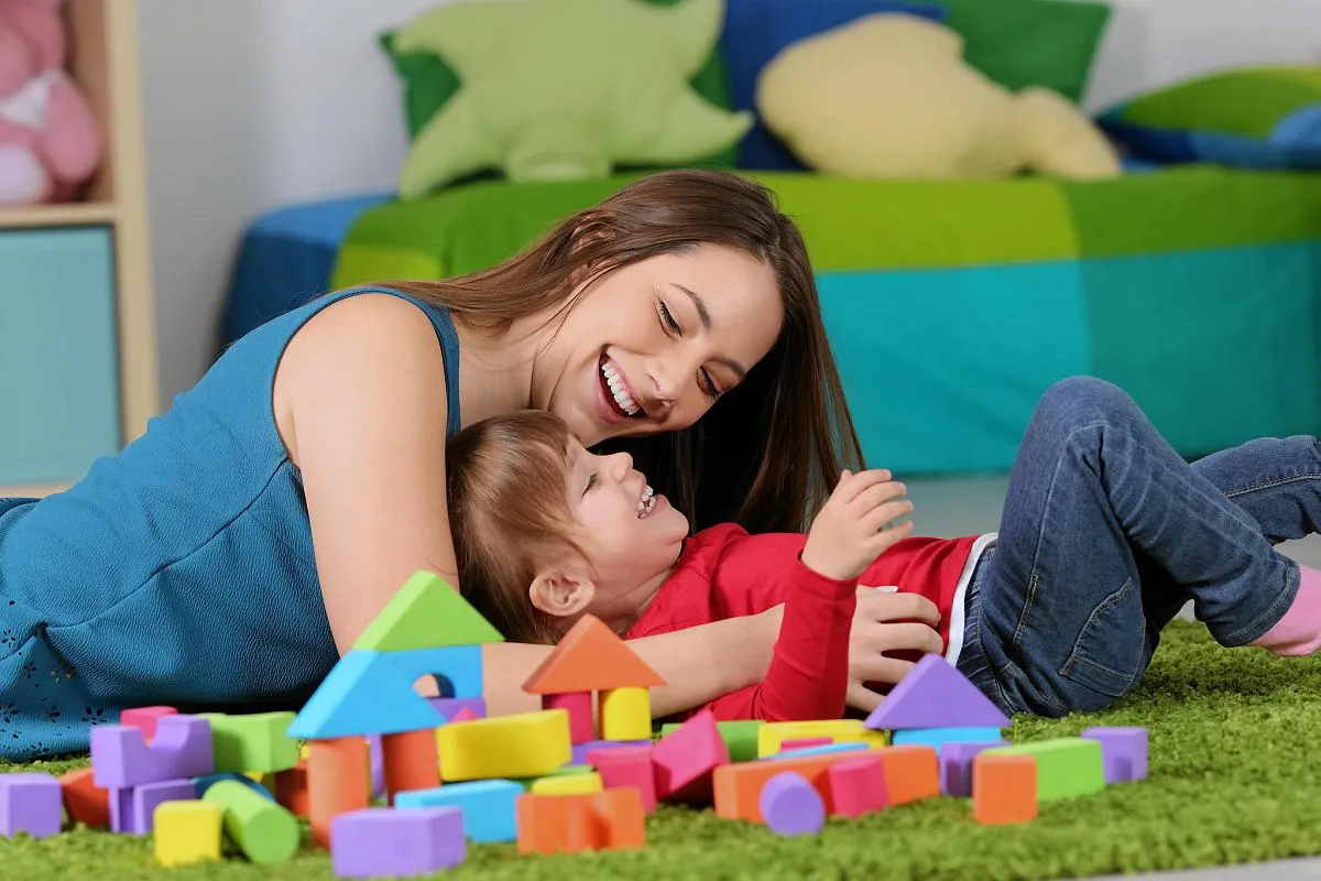 Uśmiechnięta opiekunka bawi się z dzieckiem kolorowymi klockami. To radość, która warta jest każdej ceny, gdy myślimy, ile kosztuje opieka nad dzieckiem.