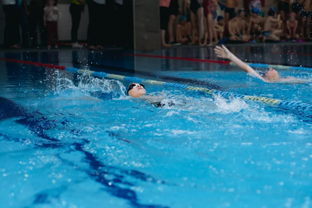 Chłopiec pływa na plecach, co jest jednym z najzdrowszych styl&oacute;w pływania. Woda rozpryskuje się wok&oacute;ł niego.