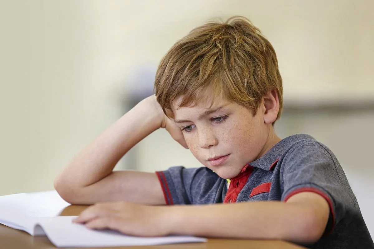 Chłopiec z piegami pochyla się nad książką, zastanawiając się, jak nauczyć dziecko czytać 8 latka.