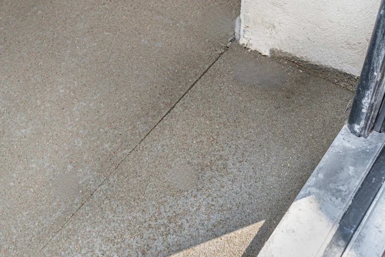 Świeżo wylany beton na podjazd, z widocznym podziałem i fragmentem ściany.