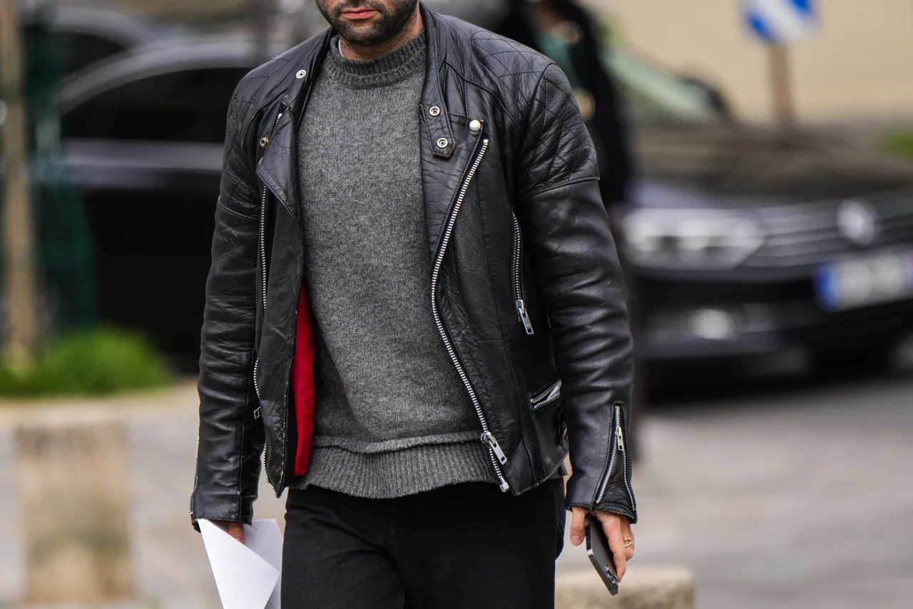 Mężczyzna w czarnej kurtce skórzanej i szarym swetrze. Idealne połączenie: jakie spodnie do kurtki skórzanej? Czarne jeansy.