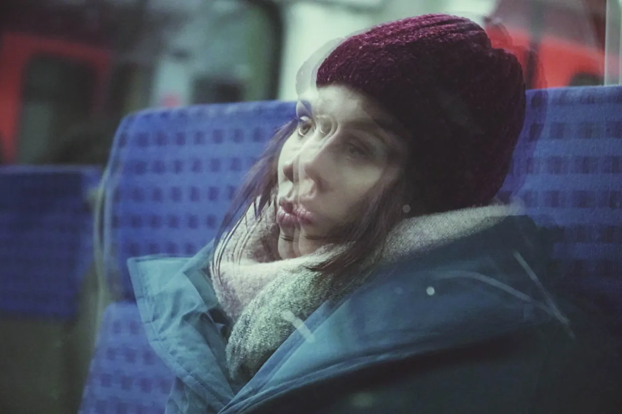 Kobieta w czapce i szaliku, siedząca w pociągu, z rozmazaną twarzą, jakby doświadczała fugi dysocjacyjnej. Czy to jej sekret, jak zostać milionerem?