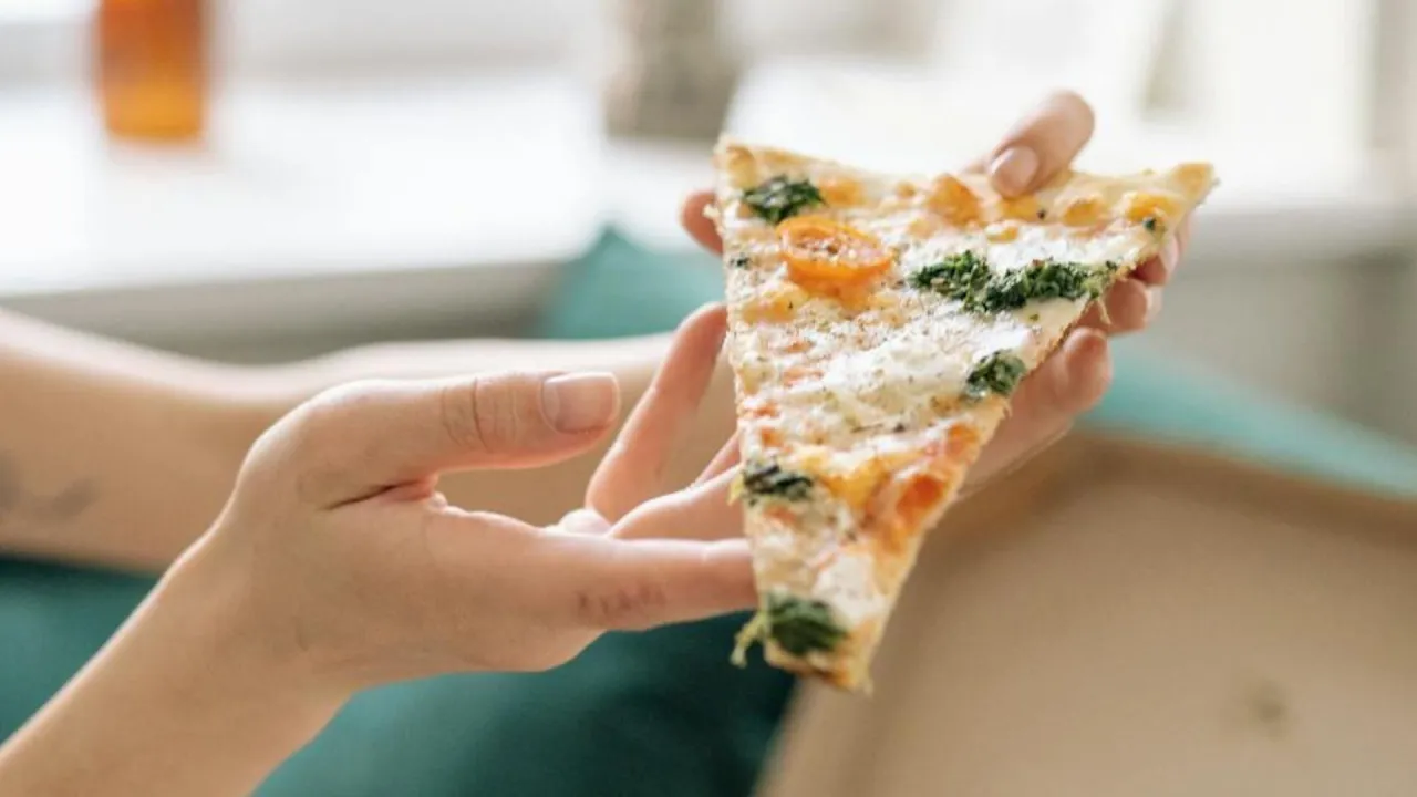 Kawałek pizzy z pomidorkami i szpinakiem, trzymany w dłoniach. Tak jeść pizzę we Włoszech &ndash; delektując się każdym kęsem.