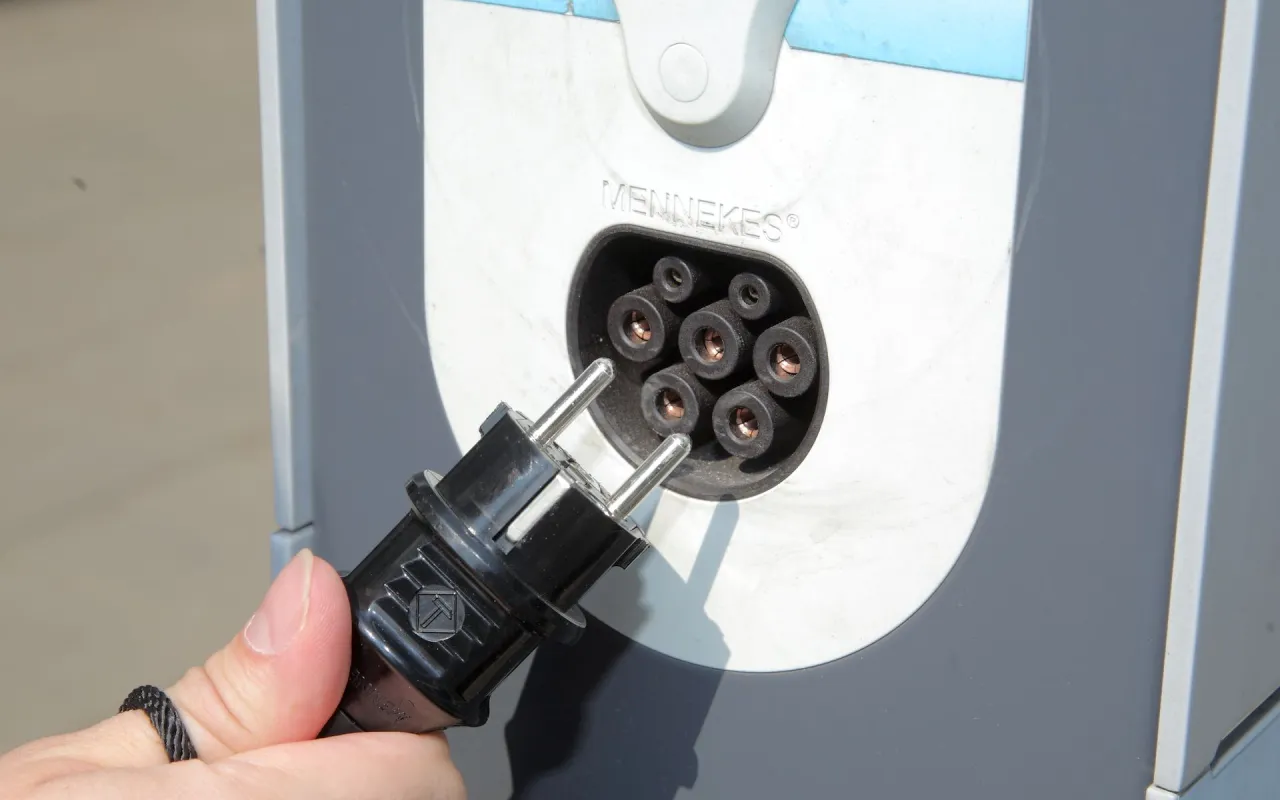 Dłoń trzyma wtyczkę, przygotowując się do podłączenia do stacji ładowania. To ważny moment, by wybrać, jaka ładowarka do samochodu elektrycznego będzie najlepsza.