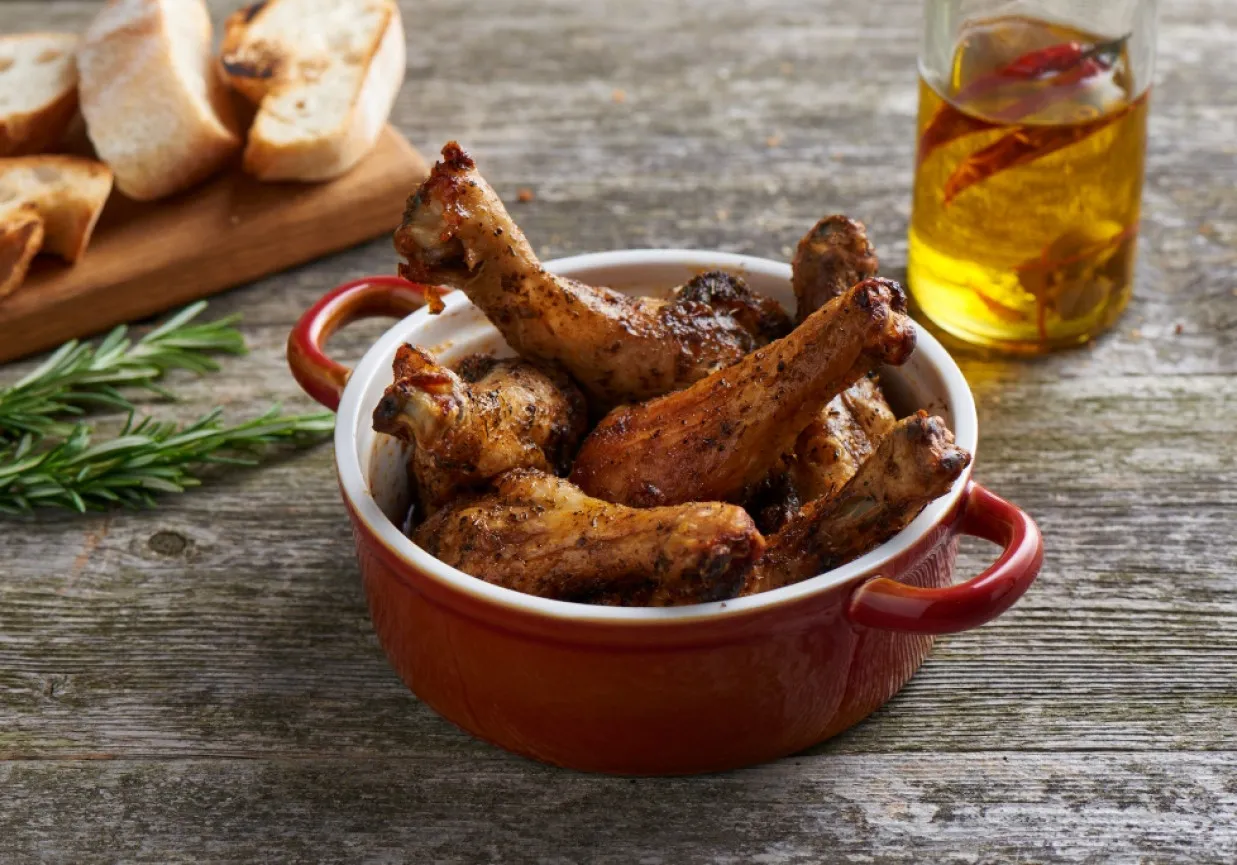 Złociste pałki z kurczaka w czerwonej miseczce, idealne do pieczenia. Obok chrupiące grzanki i oliwa z chili.