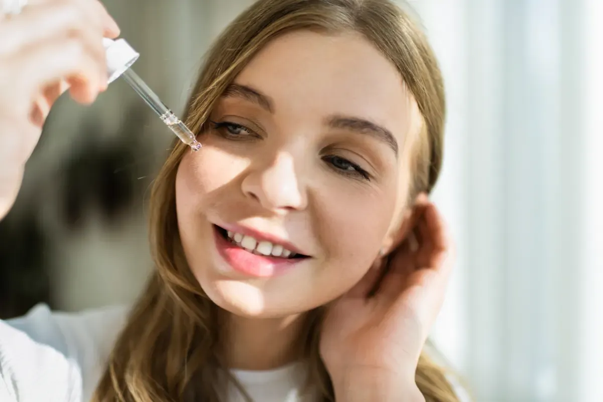 Młoda kobieta aplikuje serum na twarz. Czy kwas hialuronowy można łączyć z witaminą C? To pytanie nurtuje wiele osób dbających o cerę.