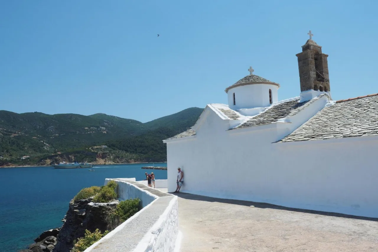 Biały kościółek na klifie, gdzie kręcono Mamma Mia. W tle błękitne morze i zielone wzgórza.