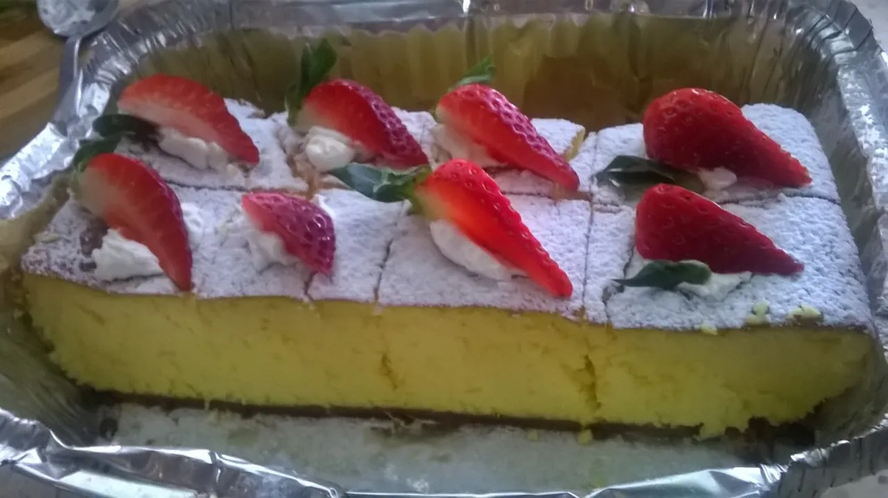 Sernik idealnie wypieczony, nie opadł! Pokrojony na porcje, udekorowany bitą śmietaną i truskawkami, posypany cukrem pudrem.