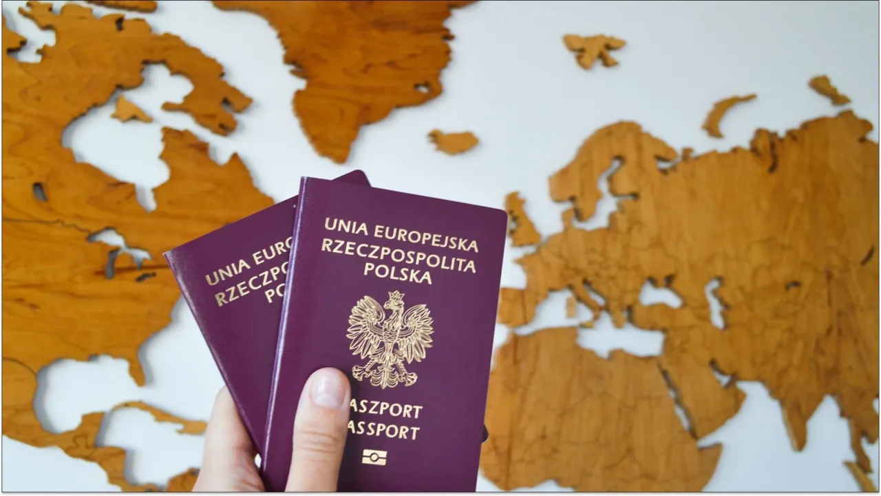 Dwa polskie paszporty w dłoni na tle drewnianej mapy świata. To wszystko, co trzeba mieć, żeby wyrobić paszport i podr&oacute;żować.