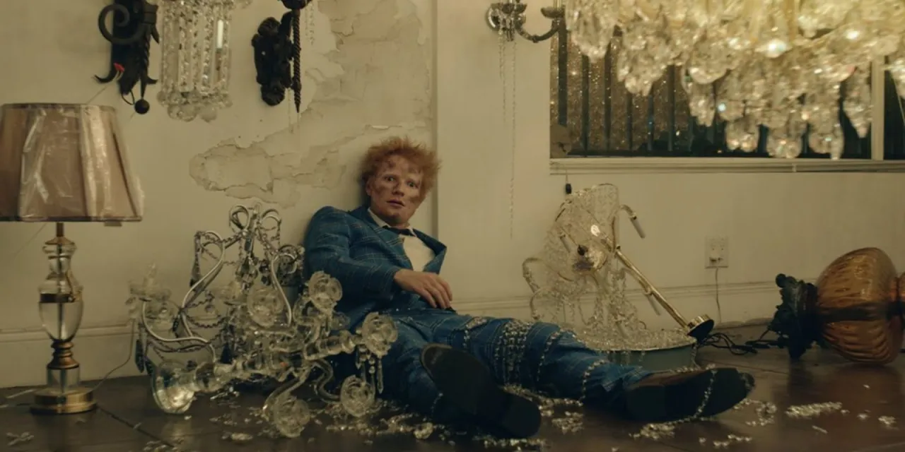 Ed Sheeran siedzi pośr&oacute;d zniszczonych kryształowych żyrandoli i lampy. Wygląda, jakby przeżył katastrofę, może to był dzień, kiedy urodził się Ed Sheeran.